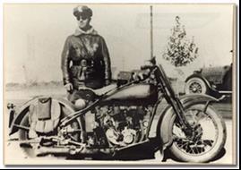 Historic department photo of a male motorcycle officer standing next to a bike