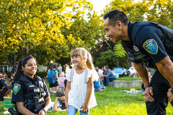 two officers smiling with a child at the park